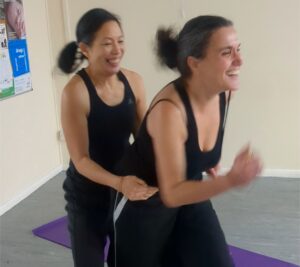 A woman is holding the waist of another woman trying to run on the spot. Both are laughing.